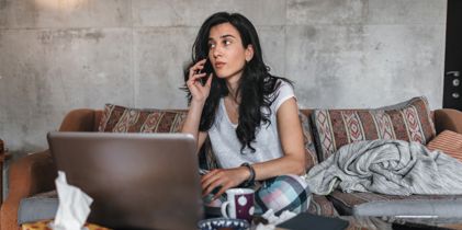 woman using phone while sitting on couch in front of laptop