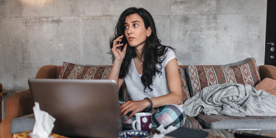 woman using phone while sitting on couch in front of laptop