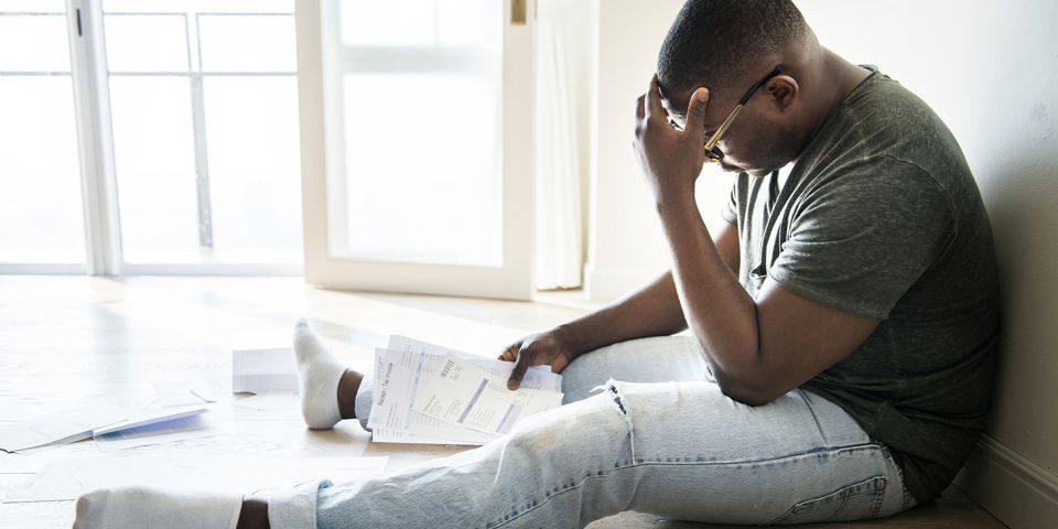 man sitting on the floor looking at all his bills